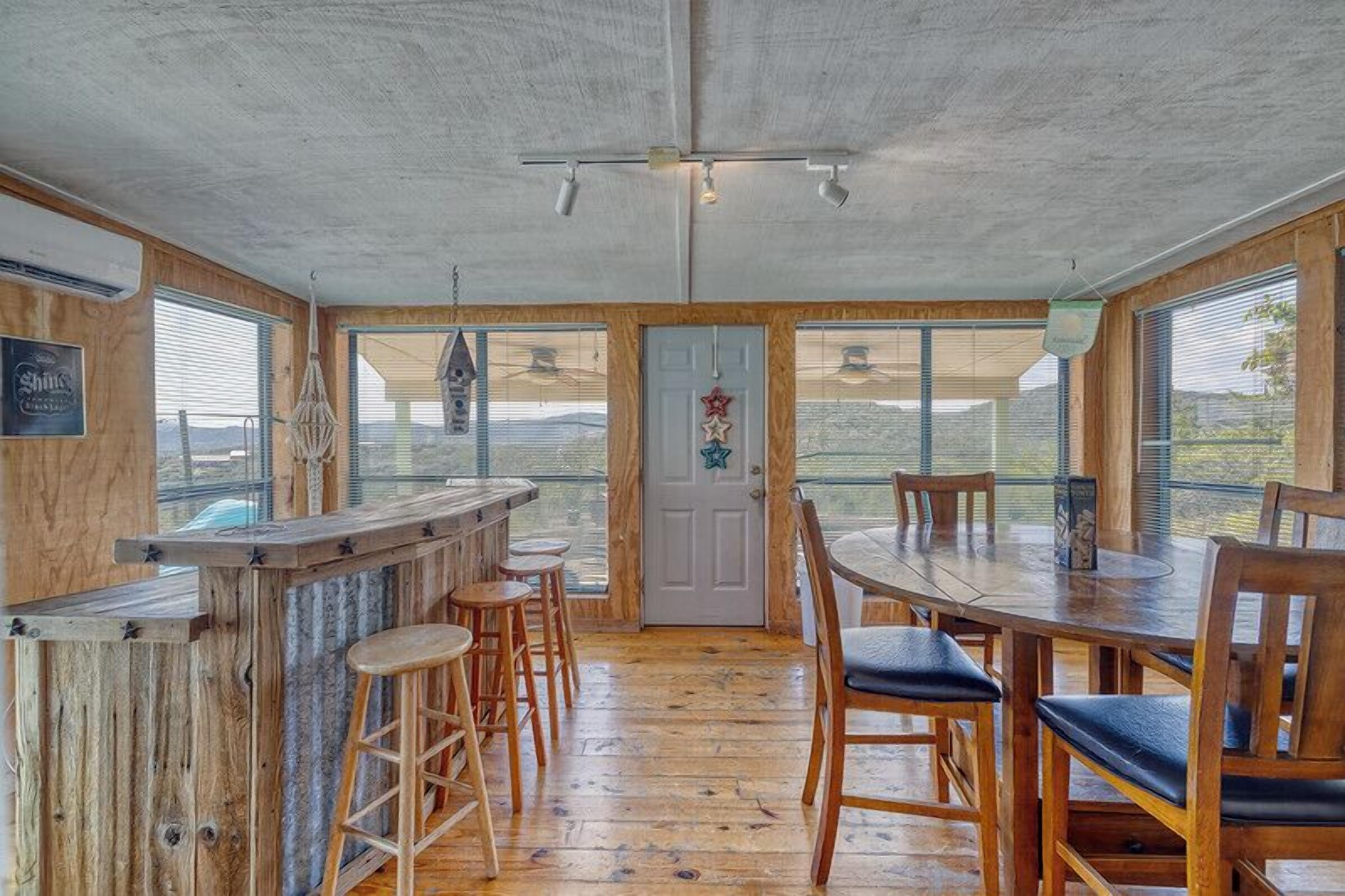 Une pièce spacieuse avec un bar en bois, un haut plafond, de grandes fenêtres et une vue sur l’extérieur.