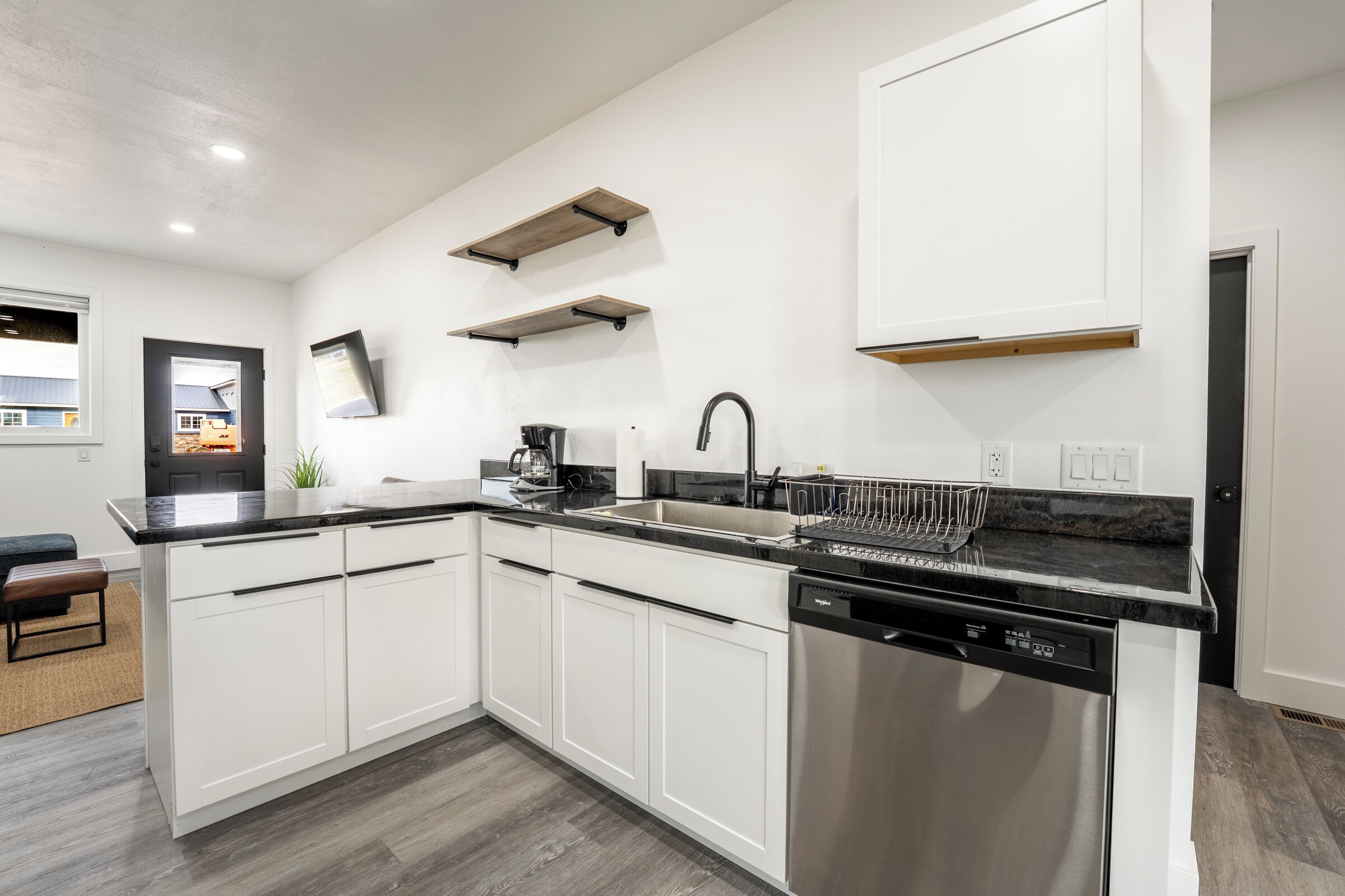A modern kitchen with white cabinets, a stainless steel dishwasher, and wooden shelves.
