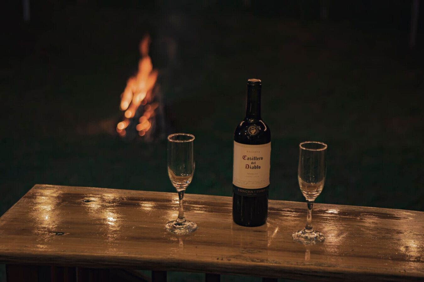 A bottle of Casillero del Diablo wine on a wooden table with two glasses.