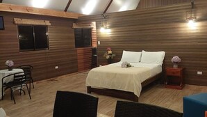Een slaapkamer in loftstijl met een schuin dak, houten wanden, een bed, een klein tafeltje en twee stoelen.