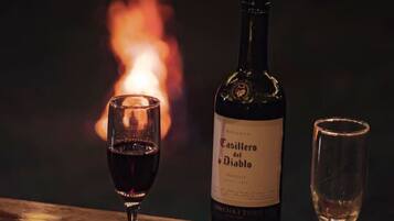 Una botella de vino Casillero del Diablo y dos copas sobre una superficie de madera, con un fuego al fondo.