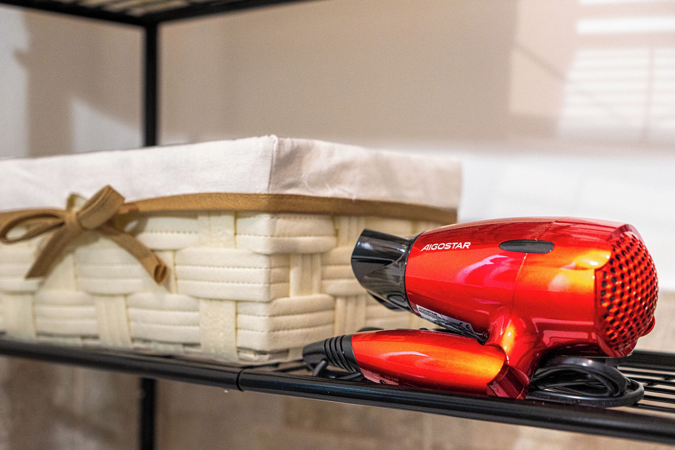 A red hair dryer and a basket of white towels on a shelf.