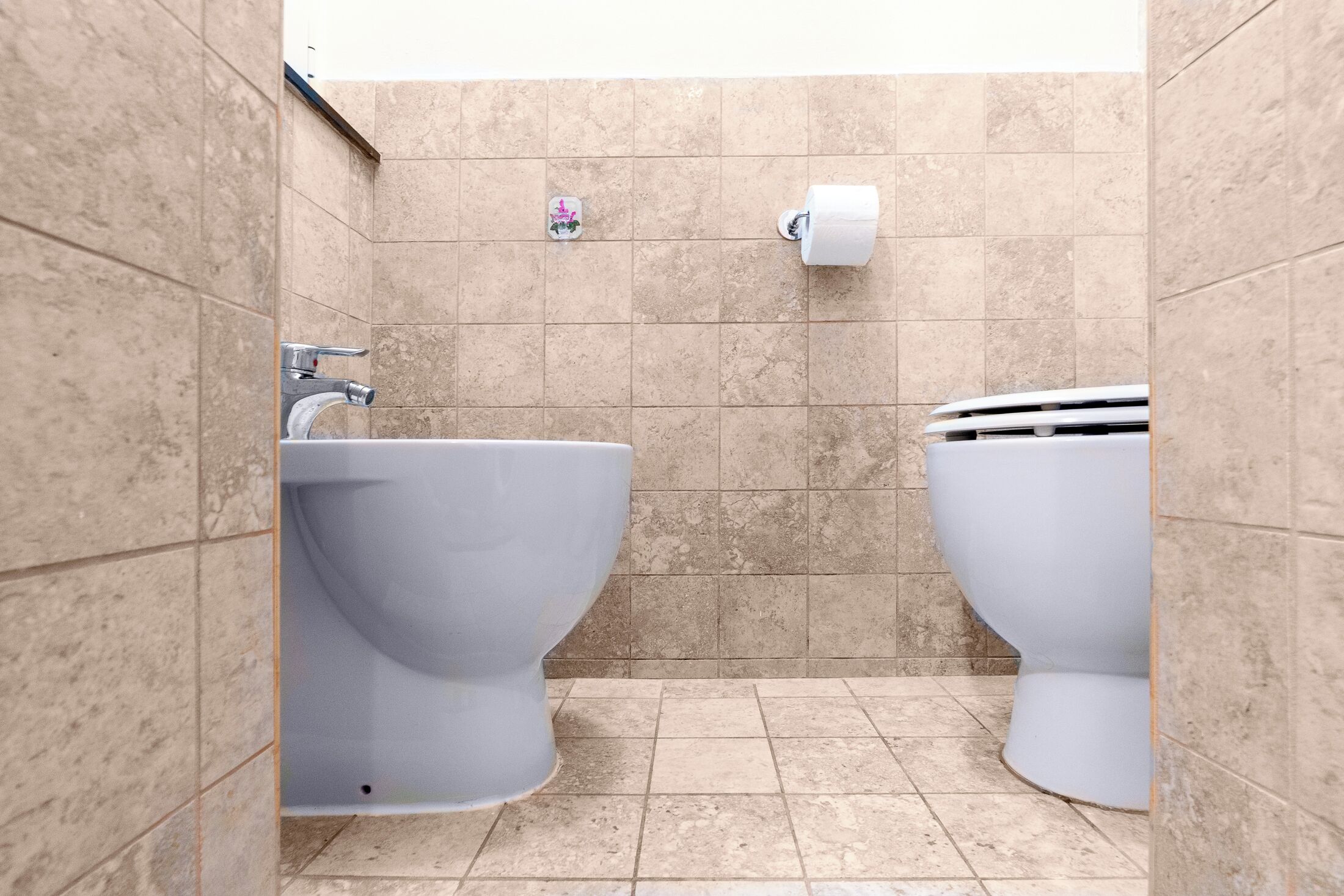 A bathroom with two toilets, a sink, and a toilet paper holder on the wall.