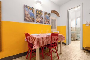 Zona pranzo con tavolo apparecchiato per quattro, sedie rosse e tre quadri appesi al muro.