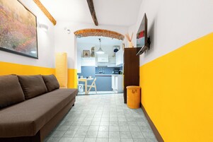 Un ambiente compatto con divano, televisore, angolo cottura e tavolo da pranzo.
