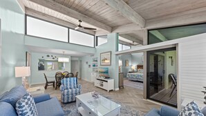 A spacious living room with a high ceiling, a glass coffee table, and blue patterned sofas.