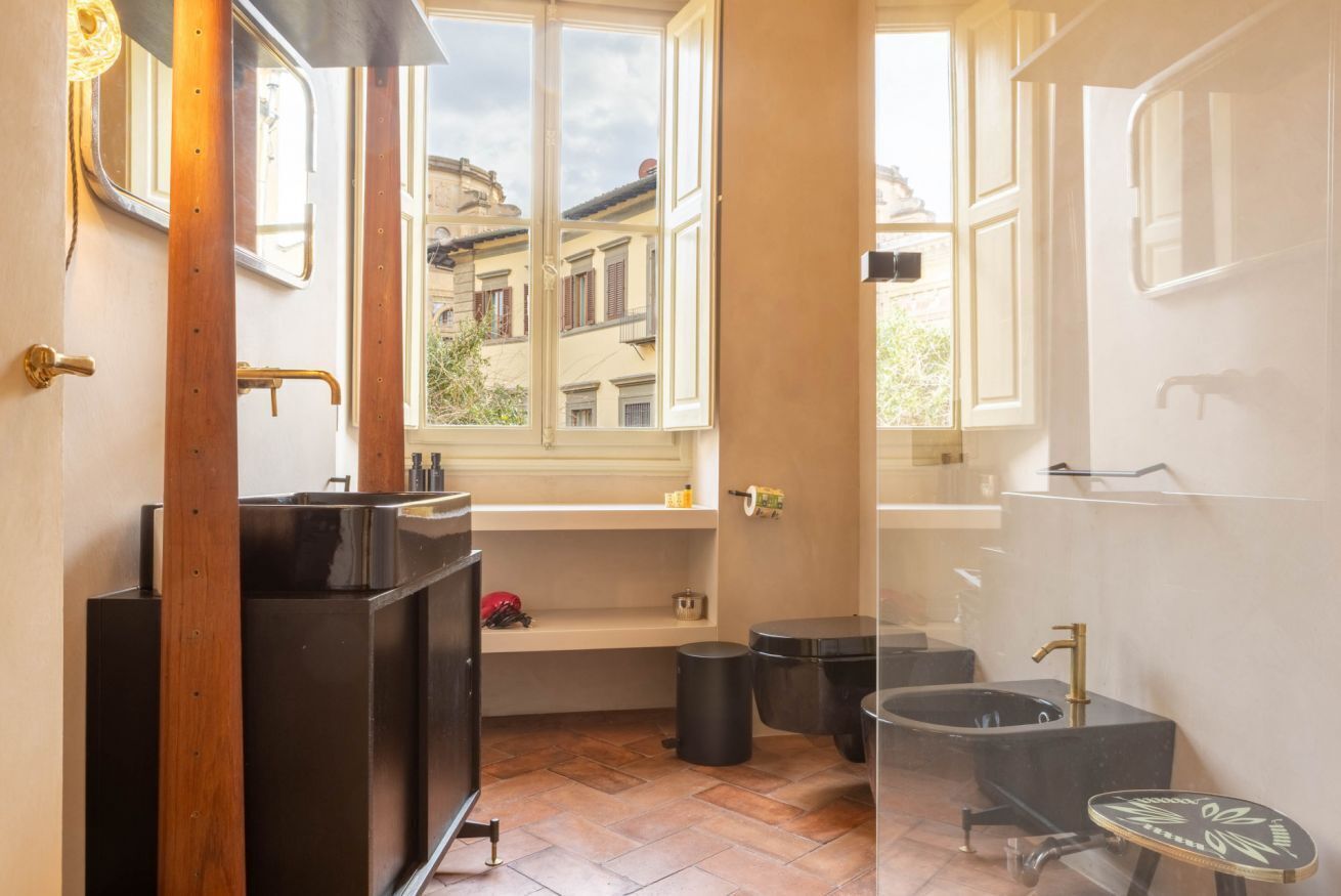 Ein kleines Badezimmer mit Fenster, einem schwarzen Waschbecken, einer Badewanne und einer kleinen Ablagefläche.