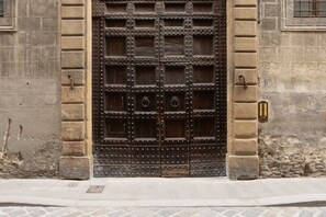 Una puerta metálica grande y ornamentada, con varios paneles y remaches, en un edificio de piedra con suelo adoquinado.