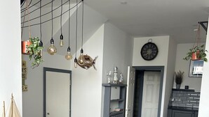 Una cocina moderna con armarios grises, una mesa de comedor de madera y un banco. Hay luces colgantes y un reloj en la pared.