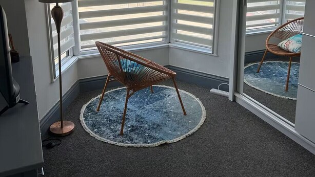 Habitación de esquina con un ventanal grande, una silla, una lámpara y una alfombra.