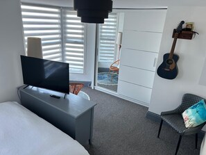 Une chambre d’hôtel avec un lit, un téléviseur posé sur un bureau, une guitare accrochée au mur et une porte coulissante donnant sur le balcon.