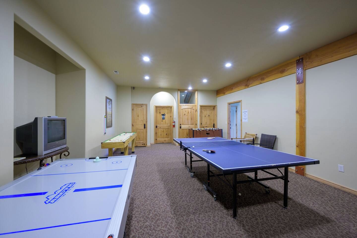 A room with two ping pong tables, a foosball table, and a television.