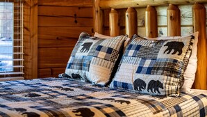 A wooden cabin interior with a bed featuring a checkered quilt and two pillows with bear designs.
