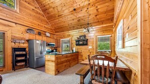 A wooden cabin interior with a kitchen, dining area, and a large window.