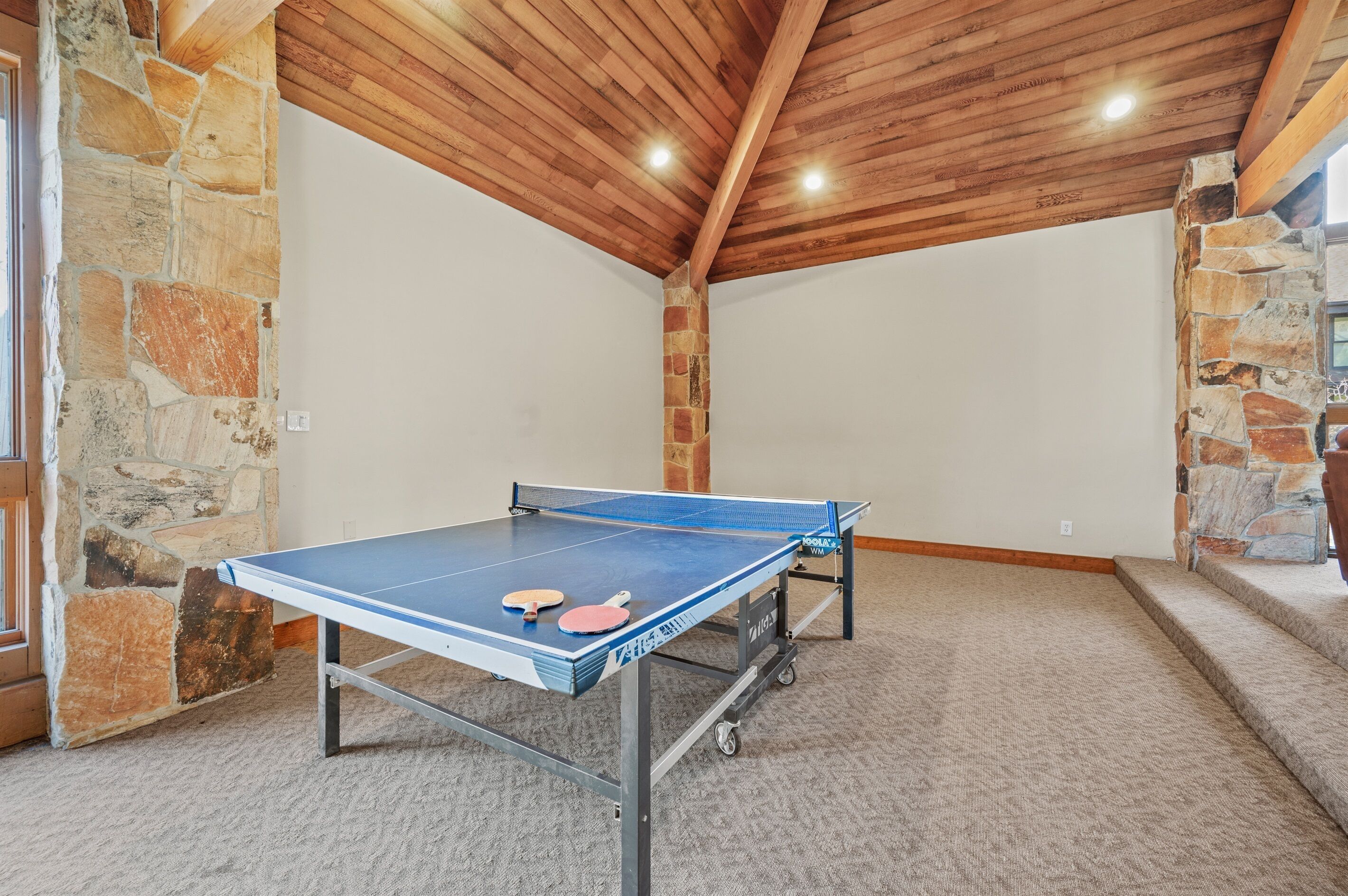 Une table de ping-pong dans une pièce aux murs de pierre et au plafond orné de poutres en bois.
