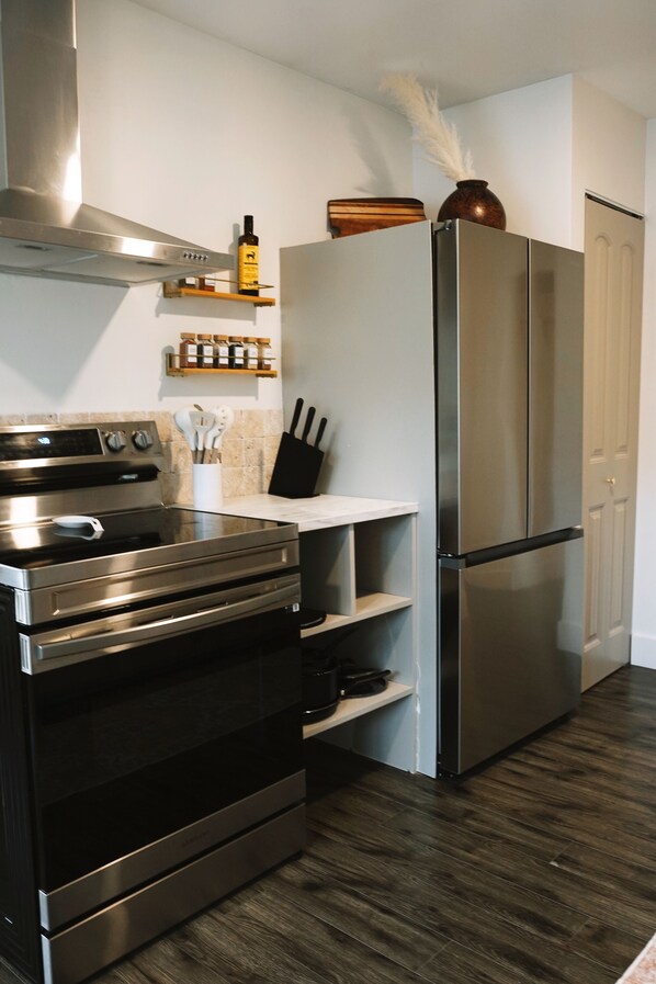 A kitchen with a stainless steel oven, a refrigerator, and a wooden shelf with kitchen utensils.
