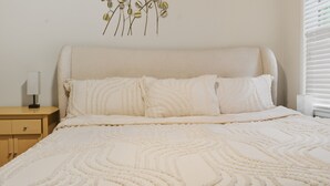 A neatly made bed with a textured blanket and two pillows, a bedside table with a lamp, and a wall-mounted decorative piece. - Charming 3-Bedroom Atlanta Retreat Near Midtown (Atlanta)