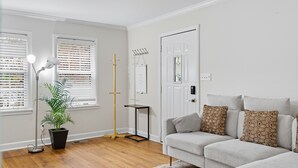 A modern living room with a grey sofa, patterned cushions, a potted plant, a floor lamp, and a wooden floor. - Charming 3-Bedroom Atlanta Retreat Near Midtown (Atlanta)