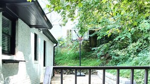 A brick pathway leading to a wooden deck with a basketball hoop, surrounded by greenery and a white building. - Charming 3-Bedroom Atlanta Retreat Near Midtown (Atlanta)