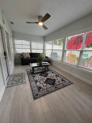A room with a ceiling fan, a sofa, a coffee table, and a window with blinds.