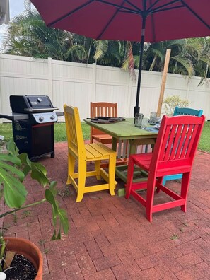 An outdoor patio with a grill, a table, and colorful chairs.