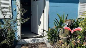 Una casa azul con puerta blanca, un camino de hormigón y plantas tropicales.