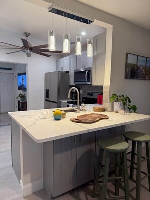 A modern kitchen with a central island, stainless steel appliances, and a ceiling fan.