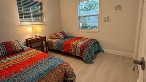 Un dormitorio con dos camas, un ventilador de techo, una ventana con persianas y una puerta.
