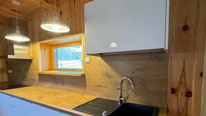 A modern kitchen with wooden walls, a window, and pendant lights.
