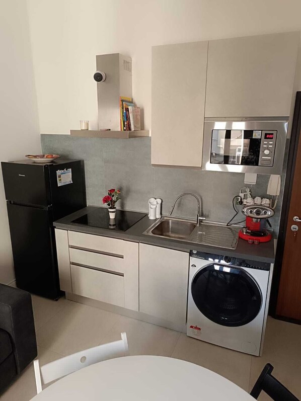 A compact kitchen with a refrigerator, microwave, sink, and washing machine.