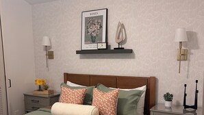 Une chambre à coucher bien rangée, avec un lit, des tables de chevet, une étagère fixée au mur et un tableau encadré.
