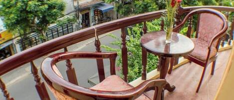 A balcony with wooden chairs and a table, a vase with flowers, and a view of the street and buildings.