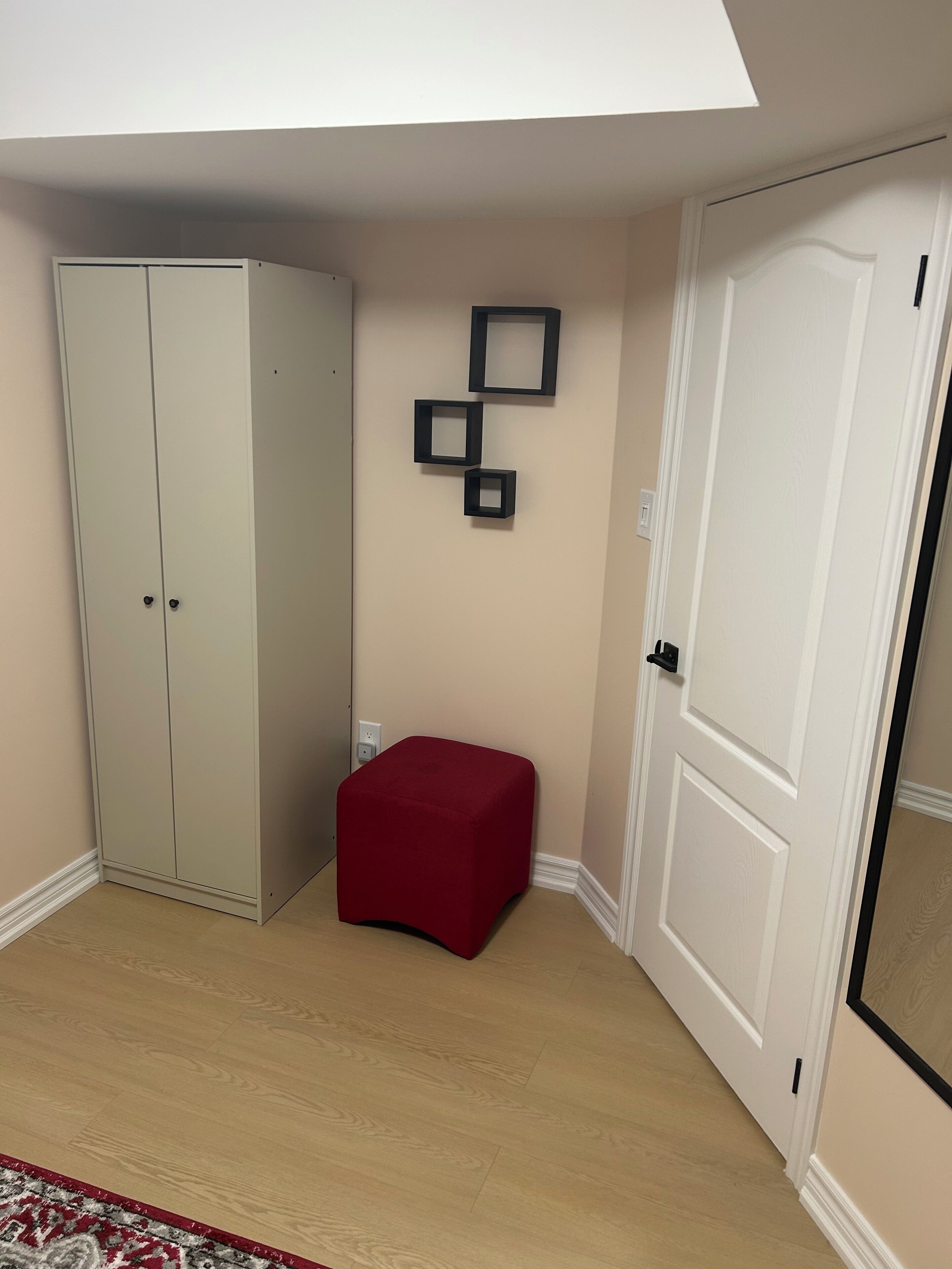 A room with a wardrobe, a red ottoman, and a door.