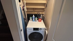 Een wasserette met een voorlader wasmachine, een droogrek en diverse schoonmaakmiddelen.