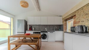 A modern kitchen with white cabinets, a washing machine, and a dining area with a wooden table and chairs.