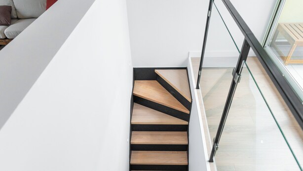 A modern staircase with wooden steps and black railings, leading to a lower level.