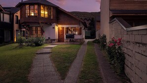 Uma casa de madeira com varanda, churrasqueira e um caminho que leva à entrada.