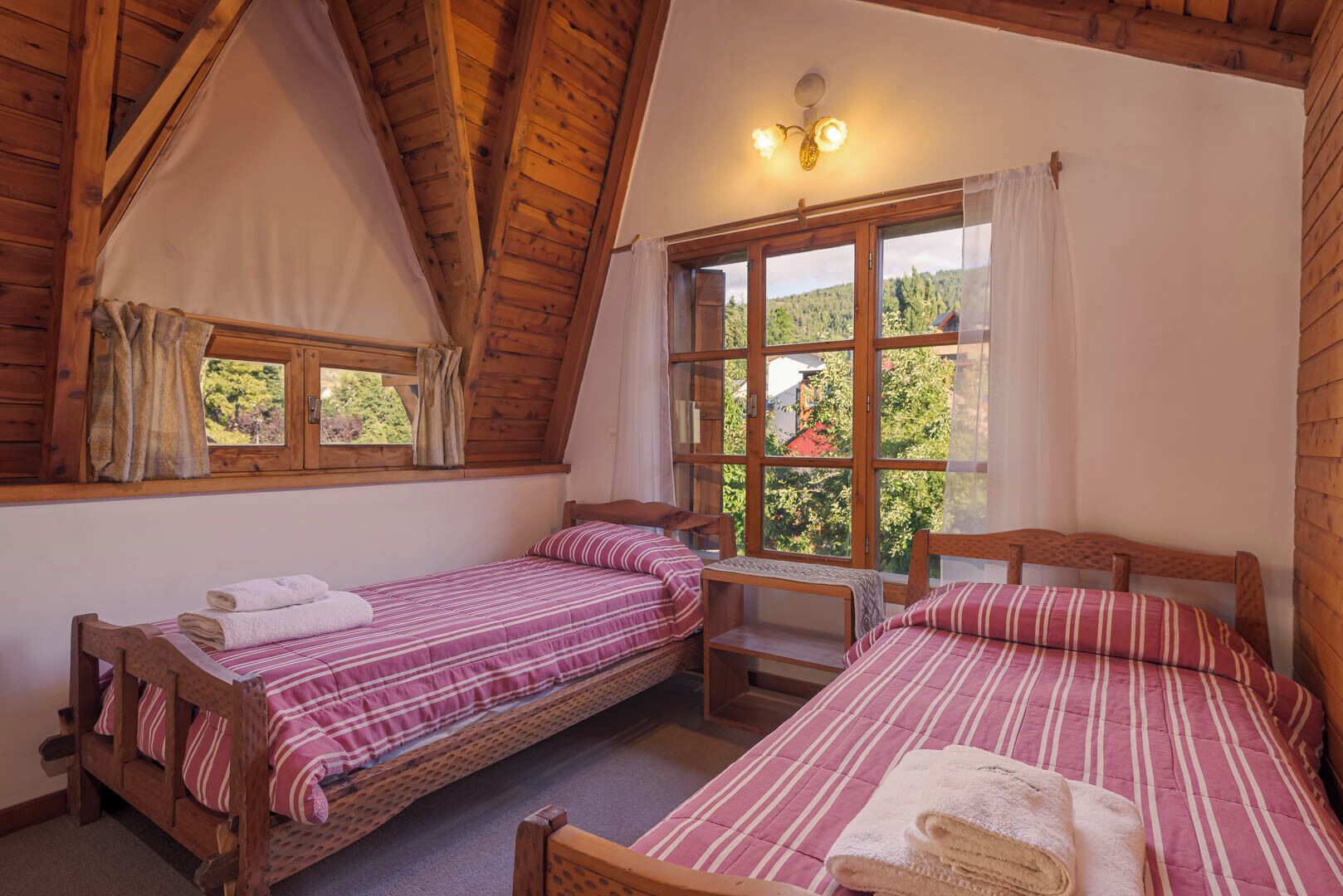 Una habitación acogedora con dos camas de madera, una ventana con cortinas y techo de madera.
