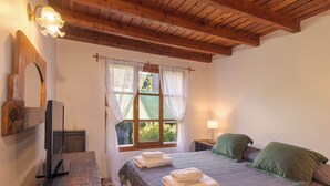 Quarto com cama, escrivaninha, luminária, janela com cortinas e teto de madeira.