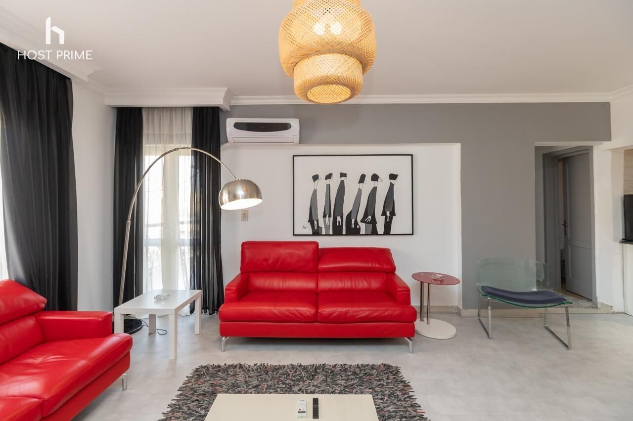 A modern living room with a red sofa, a small round table, a floor lamp, and a hanging light fixture.