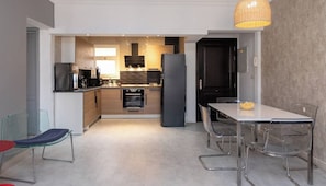 A modern kitchen with a dining area, featuring a large island, built-in appliances, and a hanging light fixture. - Luxury Apartment in Al Rehab (New Cairo)
