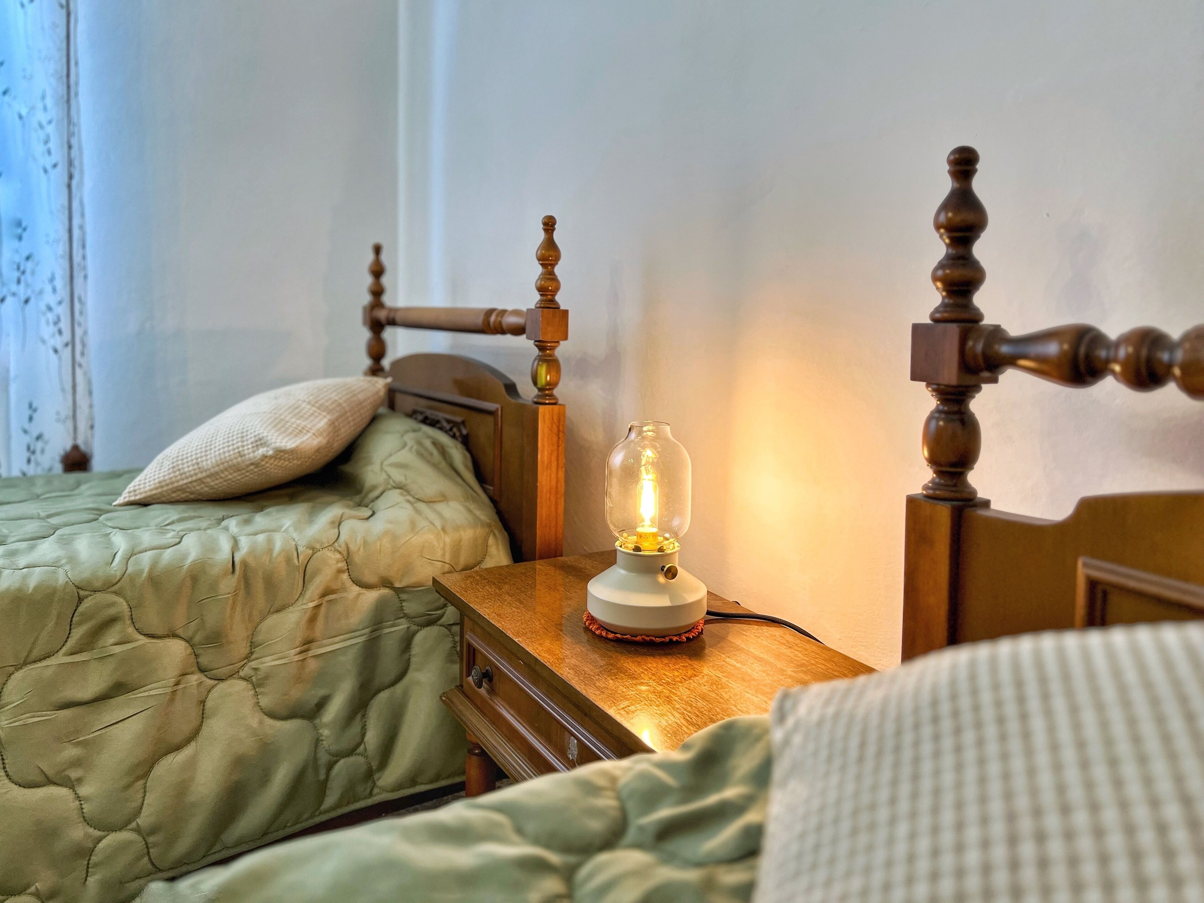 Een slaapkamer met twee bedden, een houten hoofdbord, een nachtkastje met een lamp en een raam met gordijnen.