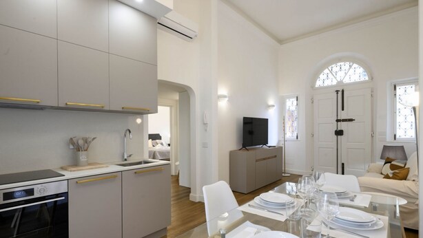 A modern kitchen with white cabinets, a built-in oven, and a dining area with a glass table set for six. - Hidden Gem with Private Garden (Firenze)