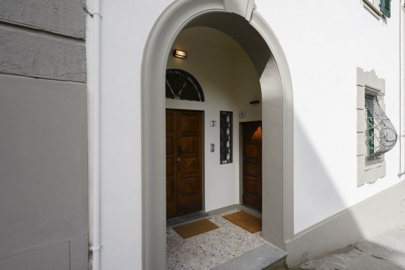 Una entrada en arco a un edificio con dos puertas de madera, con los números 7 y 9, y un pequeño ventanal con una reja de metal.