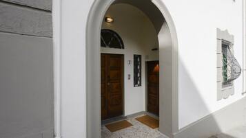 Una entrada en arco a un edificio con dos puertas de madera, con los números 7 y 9, y un pequeño ventanal con una reja de metal.