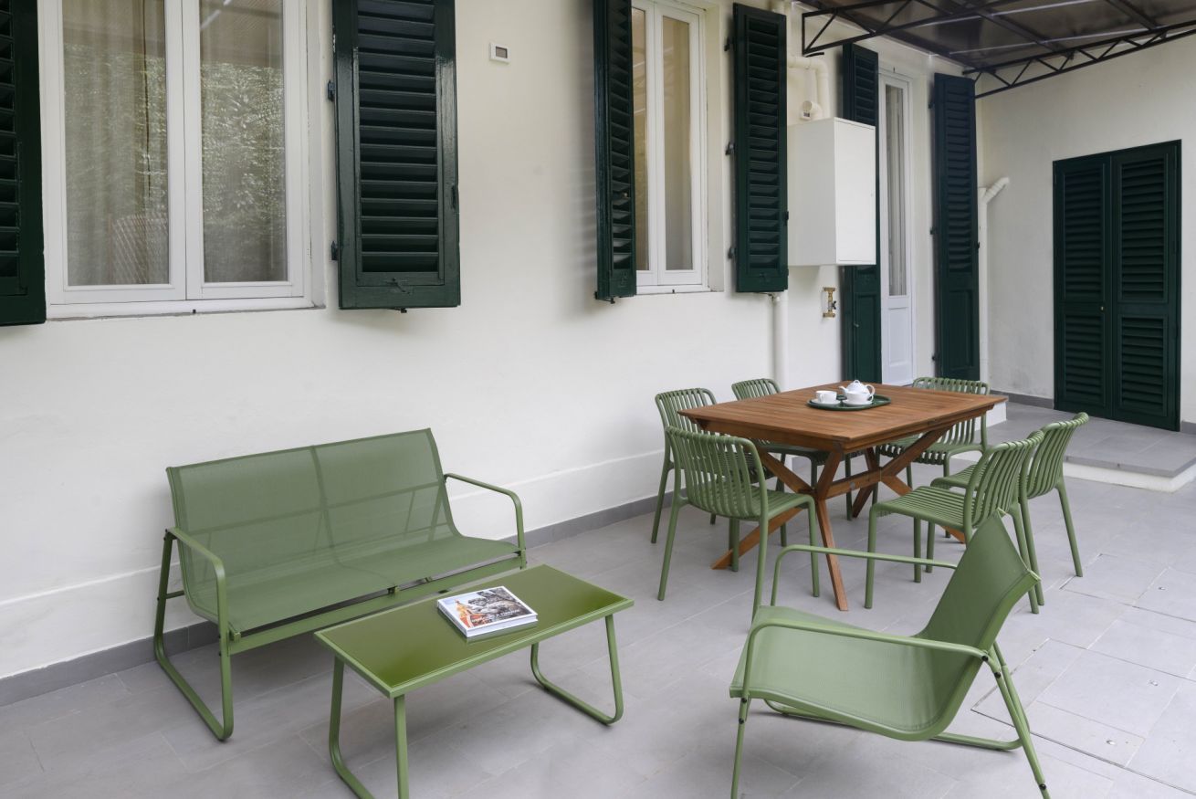 Un patio con mesa y sillas de madera, un banco verde y una mesita con una revista.