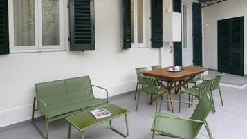Un patio con mesa y sillas de madera, un banco verde y una mesita con una revista.