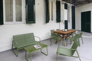 Un patio con mesa y sillas de madera, un banco verde y una mesita con una revista.