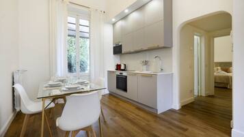 Una cocina moderna con armarios blancos, horno empotrado y una mesa de comedor de vidrio con sillas blancas.