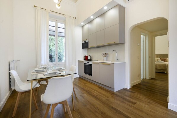 Una cocina moderna con armarios blancos, horno empotrado y una mesa de comedor de vidrio con sillas blancas.